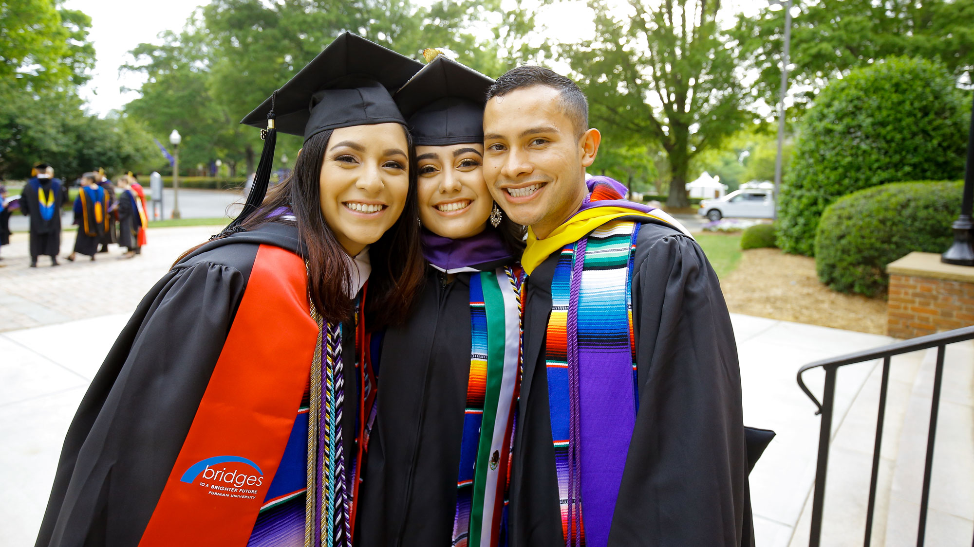Three students smiling together with robes on