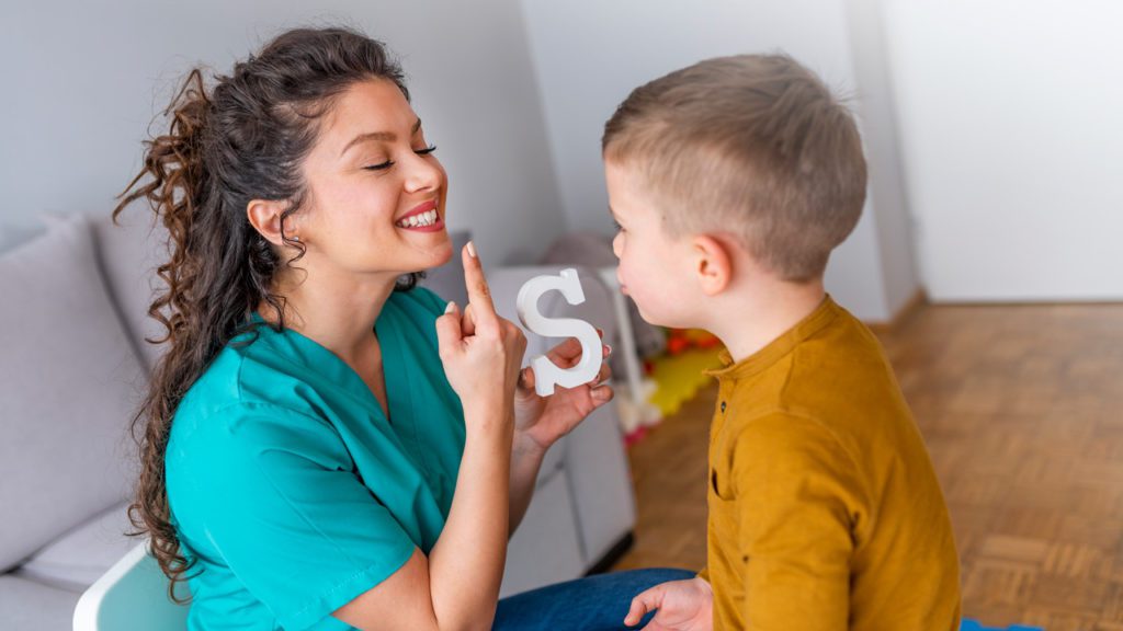 Student pointing to mouth while holding letter S