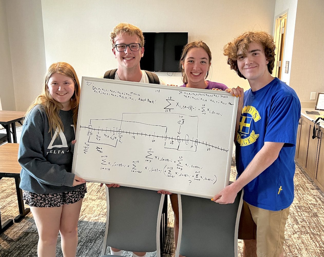 Students smiling while holding whiteboard with mathematical expressions on it.