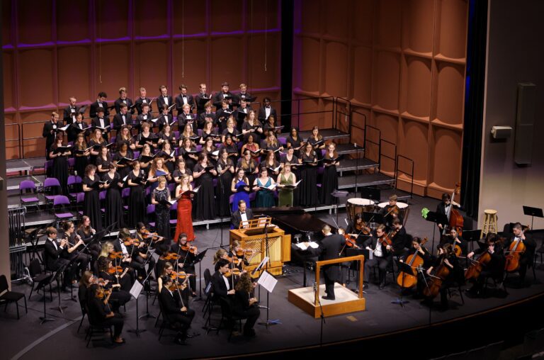 Side balcony perspective of the full Furman oratorio chorus and Furman Symphony Orchestra, performing on the McAlister Auditorium Stage for the 2022 Oratorio Concert. Several singers are in very special formalwear, because they are soloists.