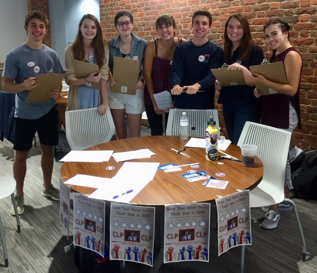 Students standing around circular table with clipboards