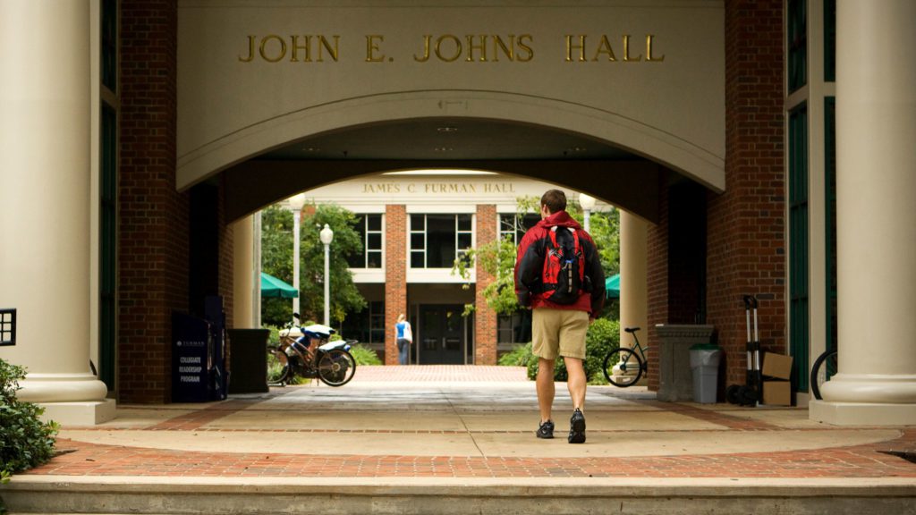 Student entering Johns Hall with backpack in tow