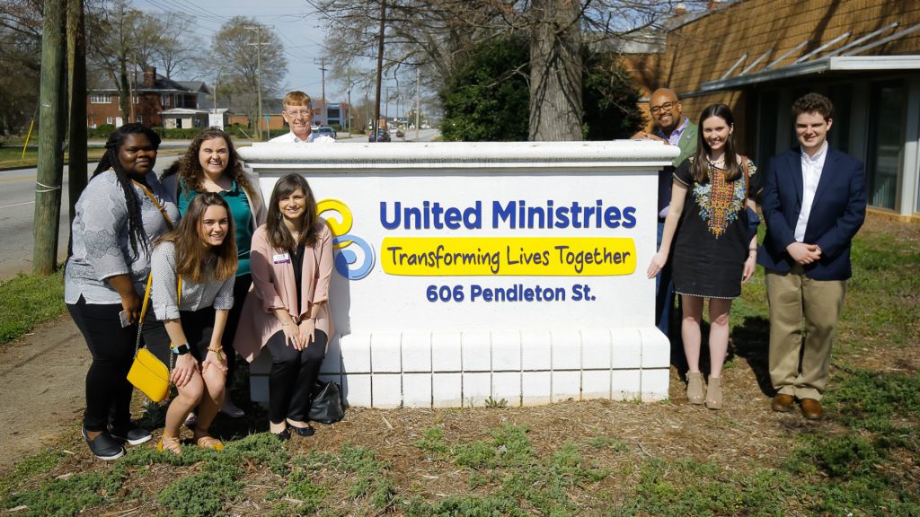 Students taking a group photo with the United Ministries sign