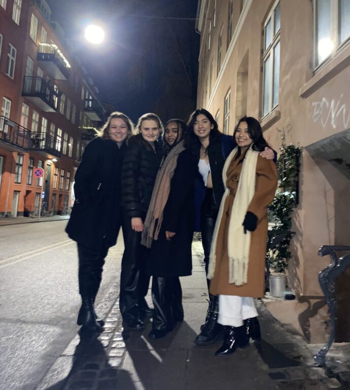 Students pose in a Danish street at night. Students are wearing jacket and scarves and are smiling.