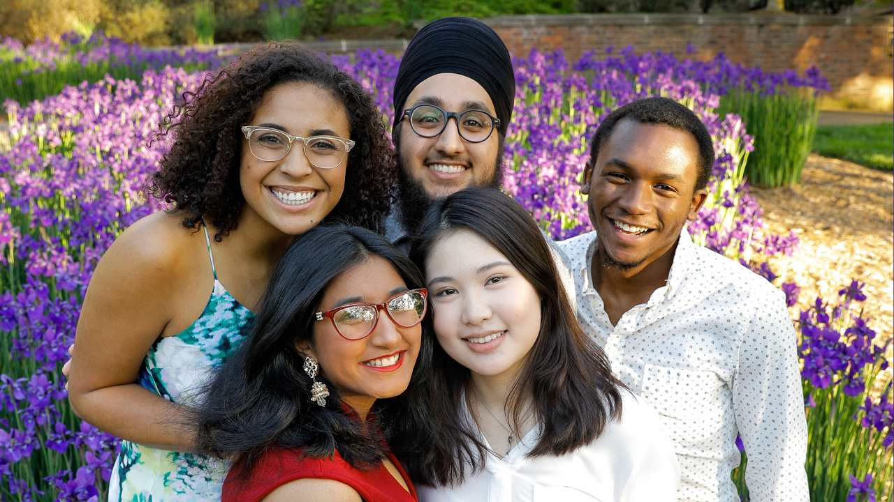Students smiling in group in front of purple flowers