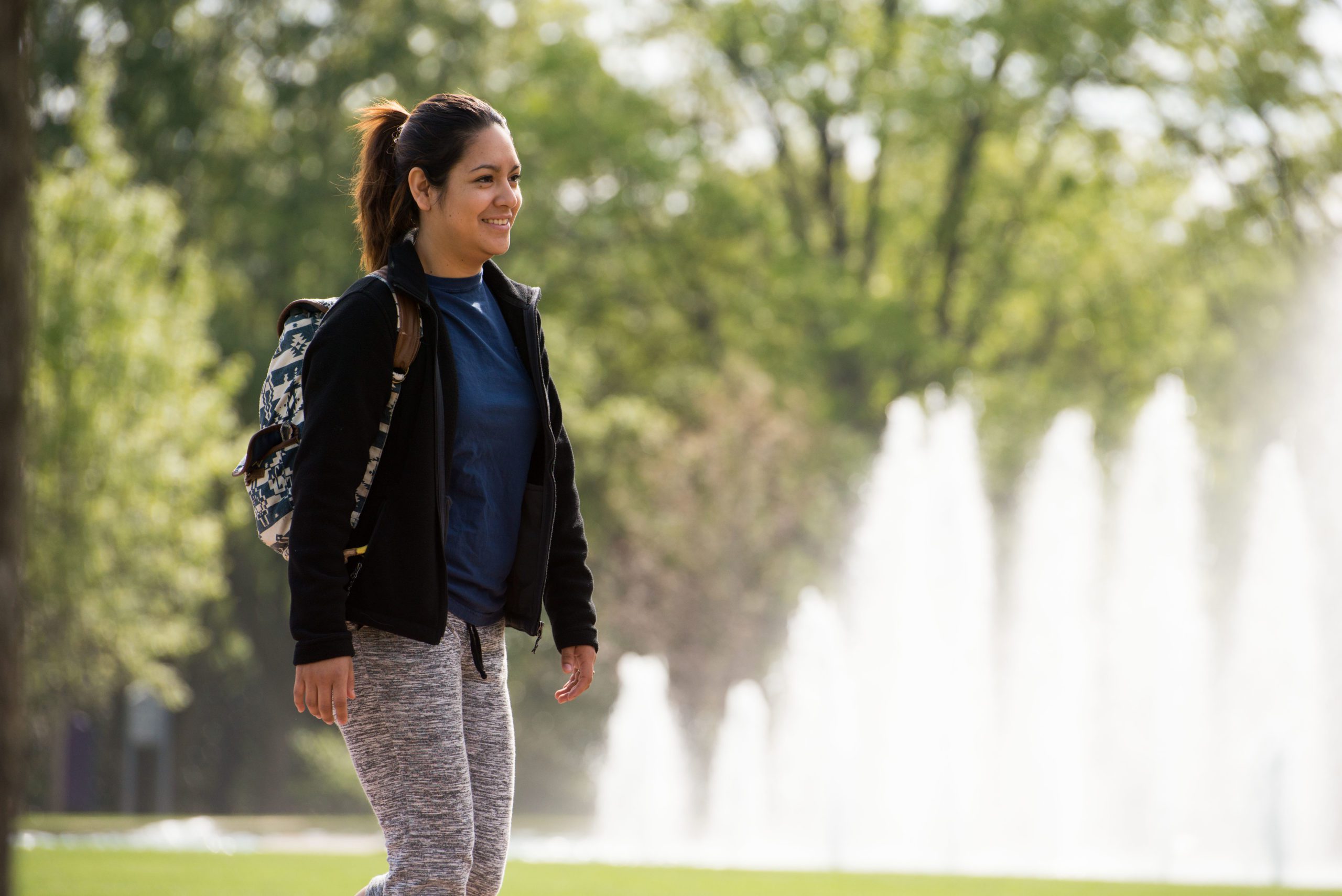 A student walks outside in front of a water fountain display on campus