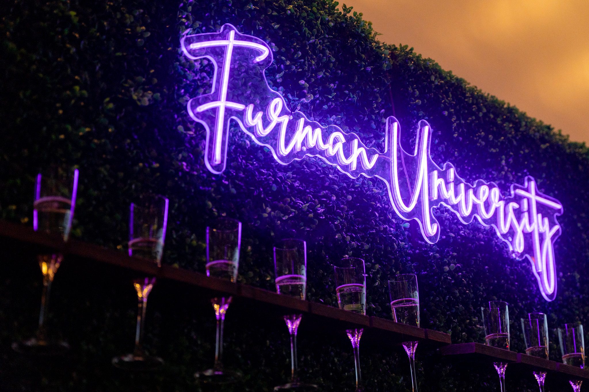 Furman University sign glows above a champaign wall
