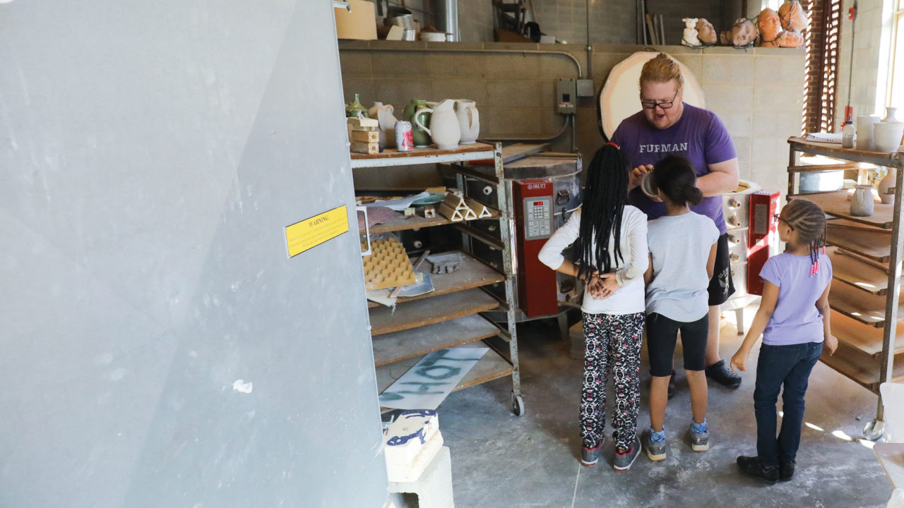 Student instructing children on creating pottery