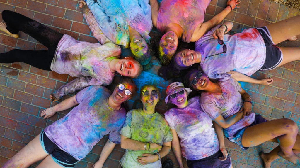 Students covered in paint from Holi Festival, laying on brick ground