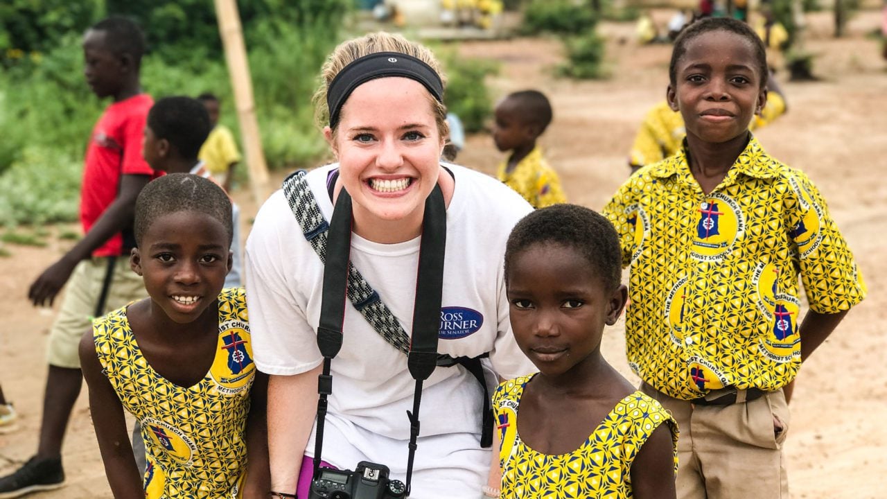 Student attending May X in Ghana, pictured with children