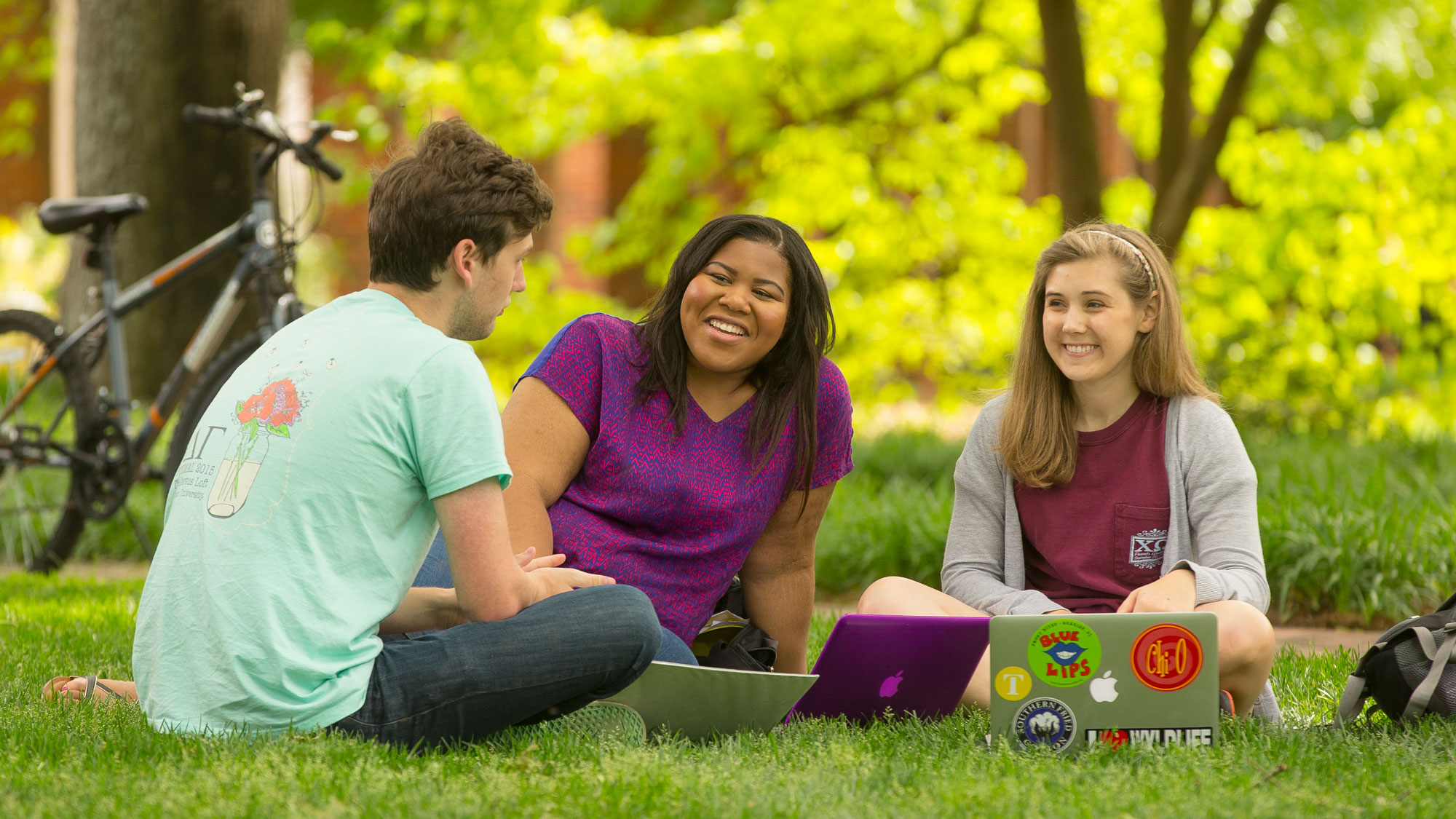 Students sitting outside in the grass with laptops