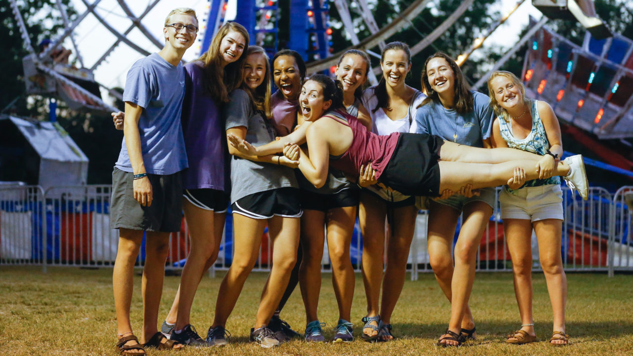 students holding a girl up in front of a Ferris wheel