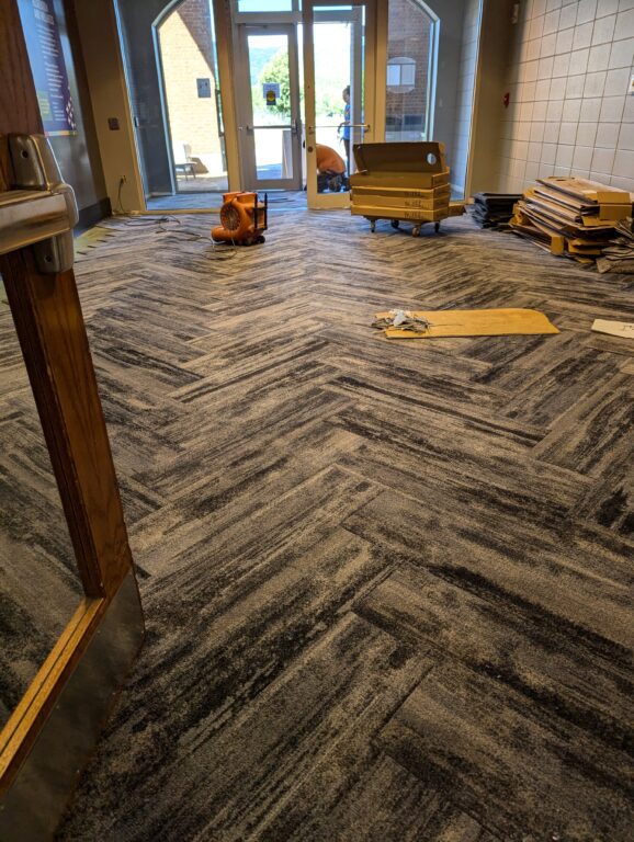 A herringbone pattern of carpet is being laid in the lobby of the PAC.