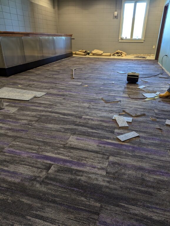 Flooring scraps are strewn about a new carpet floor with subtle hints of purple streaks.