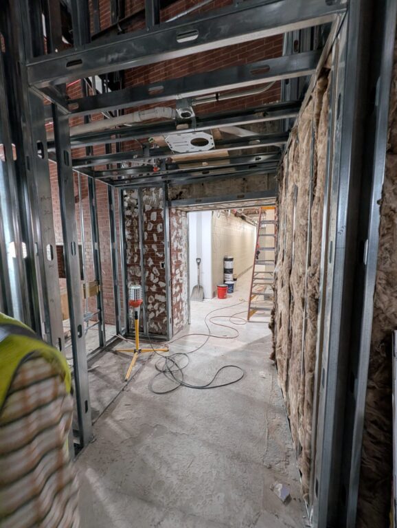 A narrow shot shows a long hallway with an outcove on the left and various doorways throughout.