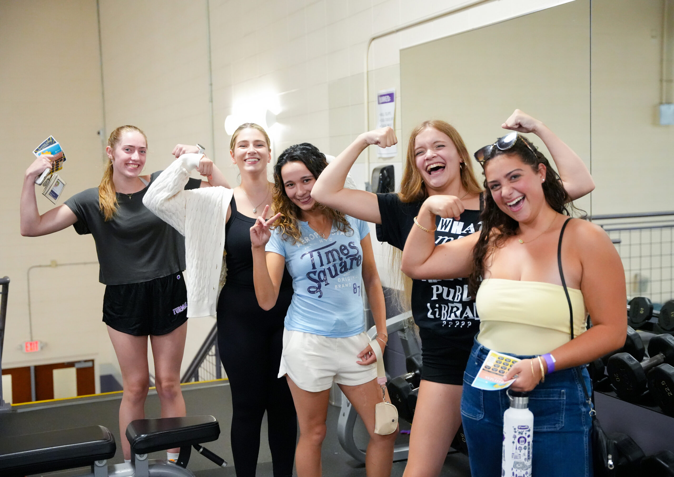 A group of women flex in the fitness center.