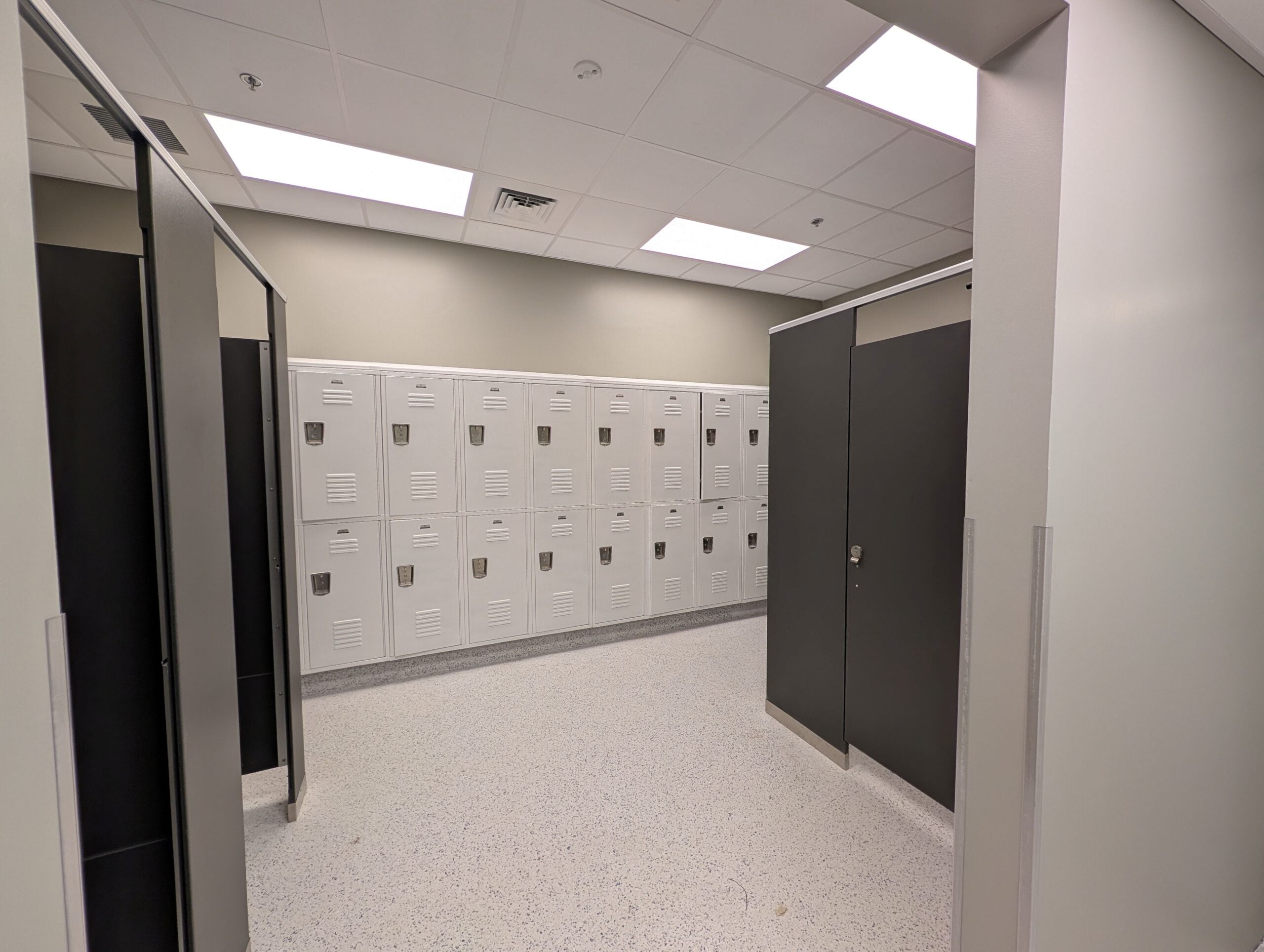 A wide angled picture shows the lockers in the background with private changing spaces flanking on either side in the foreground.