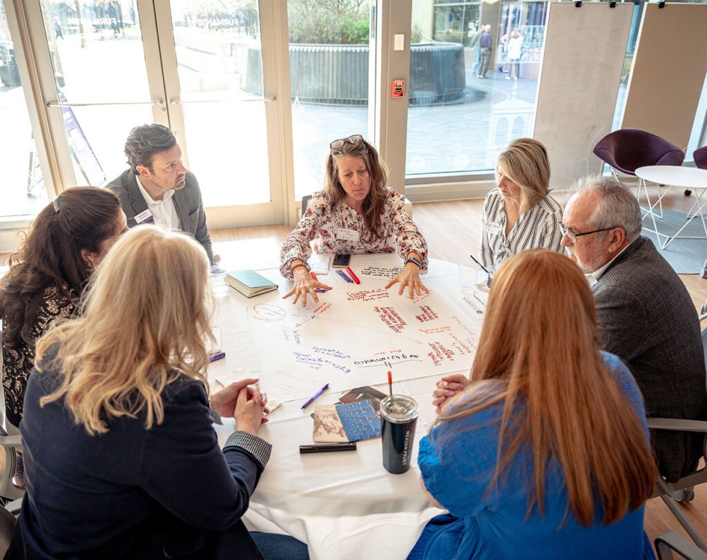 a group of men and women brainstorm on a poster board around a table