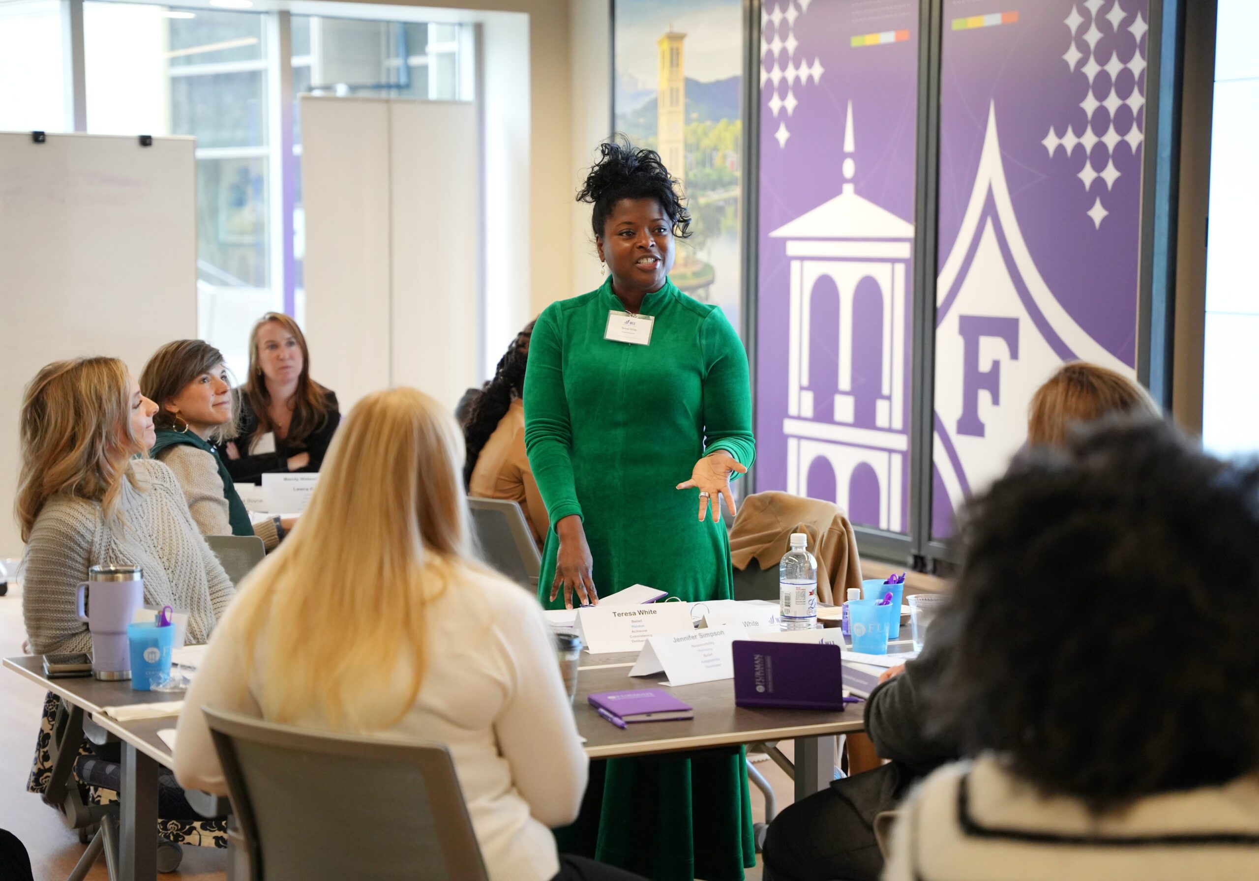 A group of women listen to one lady standing up providing explanation