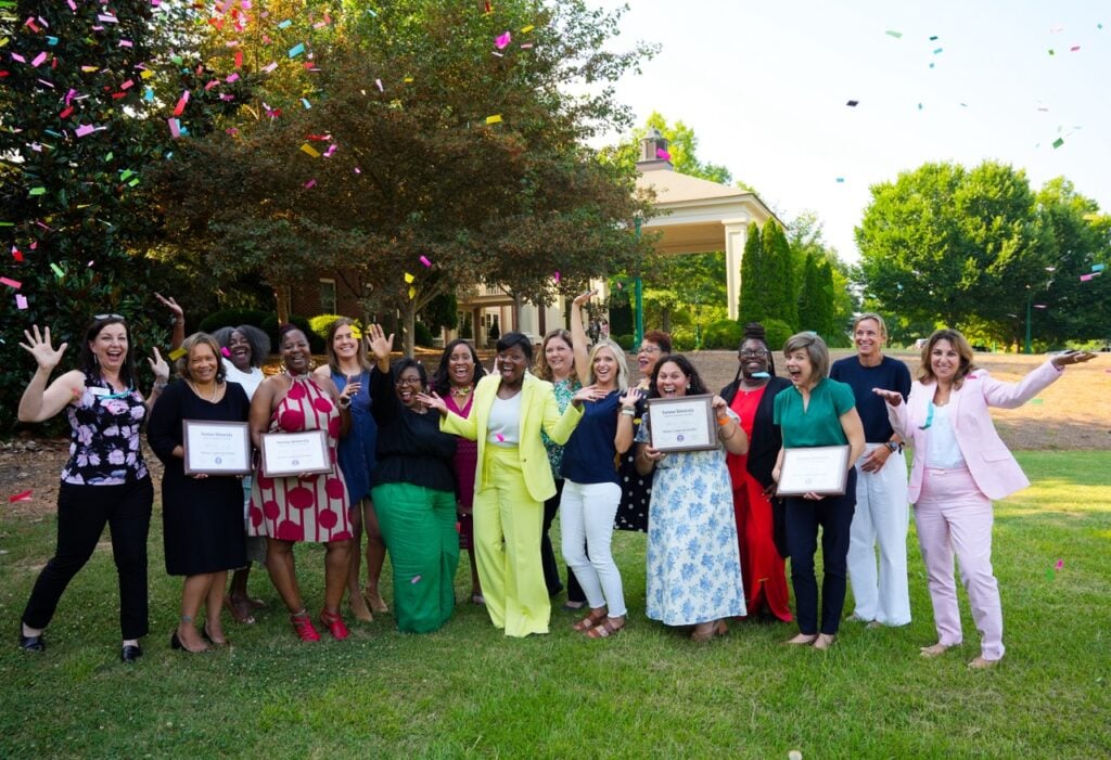a group of around seventeen women are all holding diplomas and being showered in confetti