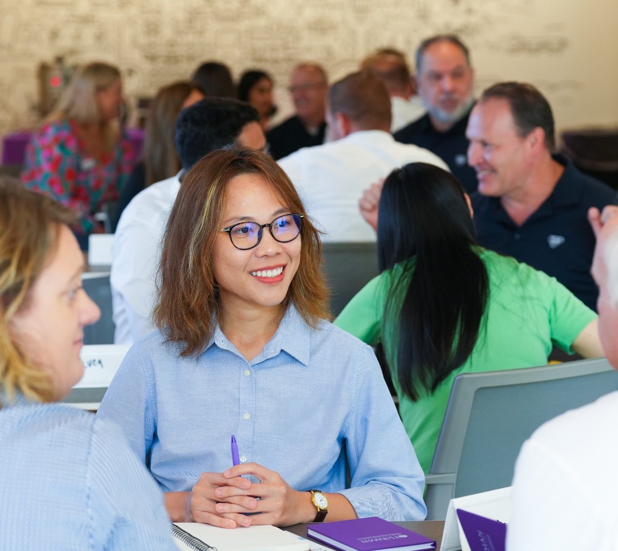 A woman in a blue shirt is listening and smiling to the other two members of the table that they are sitting at