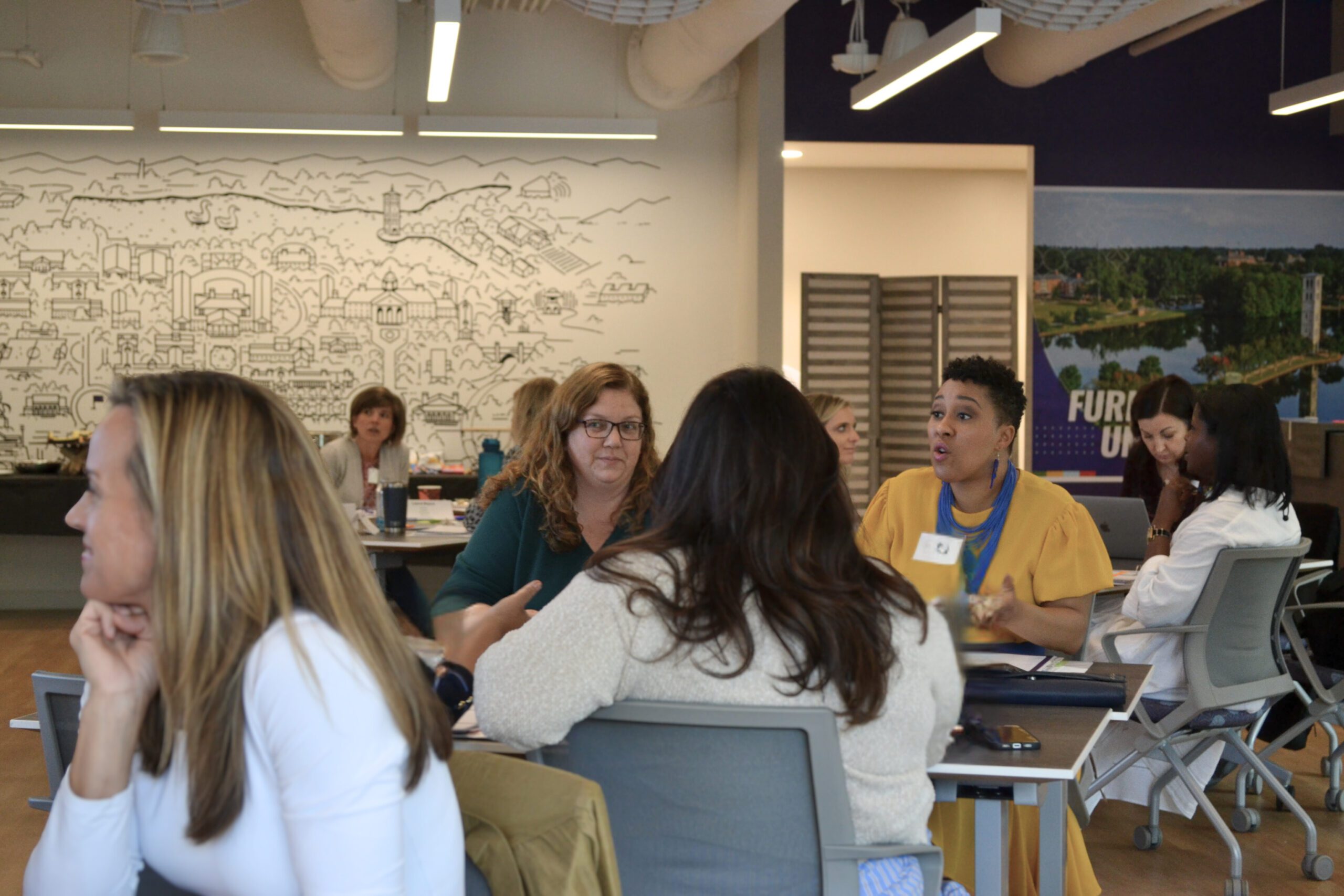 a full room of women are sitting at different tables at different intervals, discussing together at each