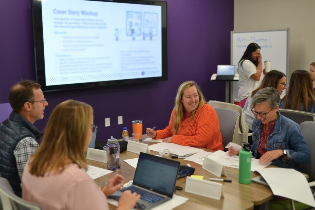 A room with pods of four people seated at each table are all working individually on projects but speaking and laughing collaboratively.