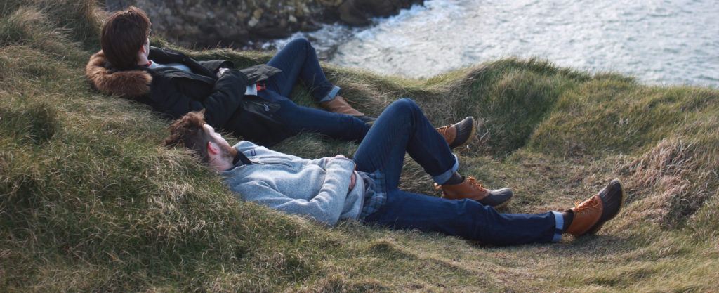 Two male students lying on the grass beside the ocean in Ireland.