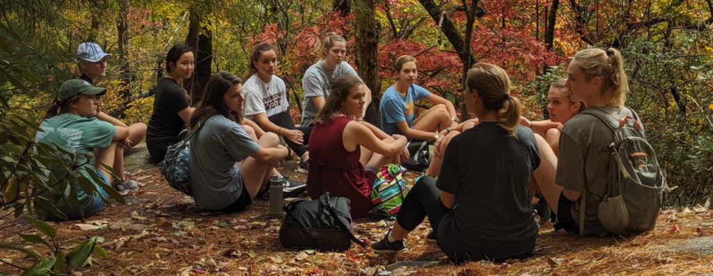 Students sitting in the woods on a hiking trail.