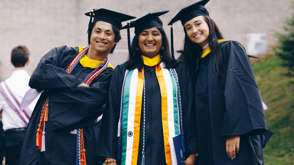 Group of three students smiling with their graduation garbs on