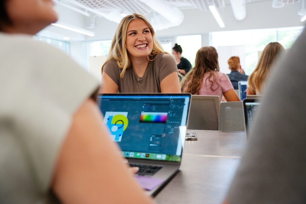 Furman Strategic Design student smiling while other student on computer.