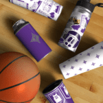 Basketball on a wooden gym floor alongside several purple-and-white branded tumblers and water bottles arranged diagonally.