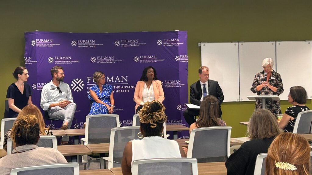 Panelists speaking at an event in front of group of attendees.