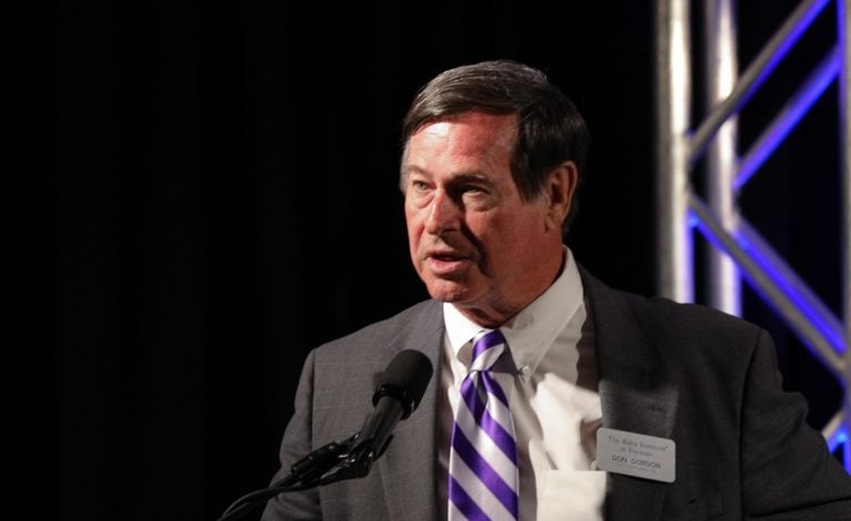 A white man in a suit speaks at a lectern. 