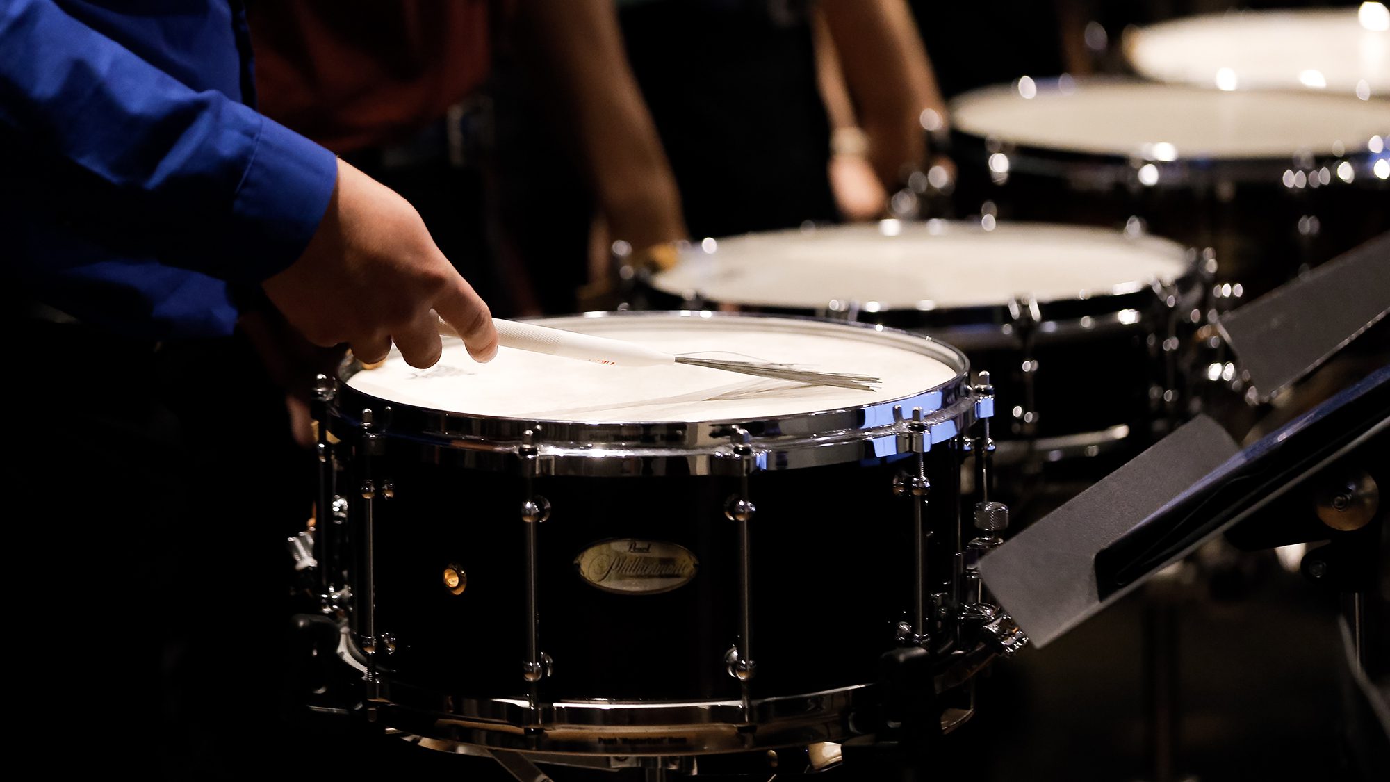 Four pairs of hands holding drumsticks play on four snare drums|Omar Carmenates