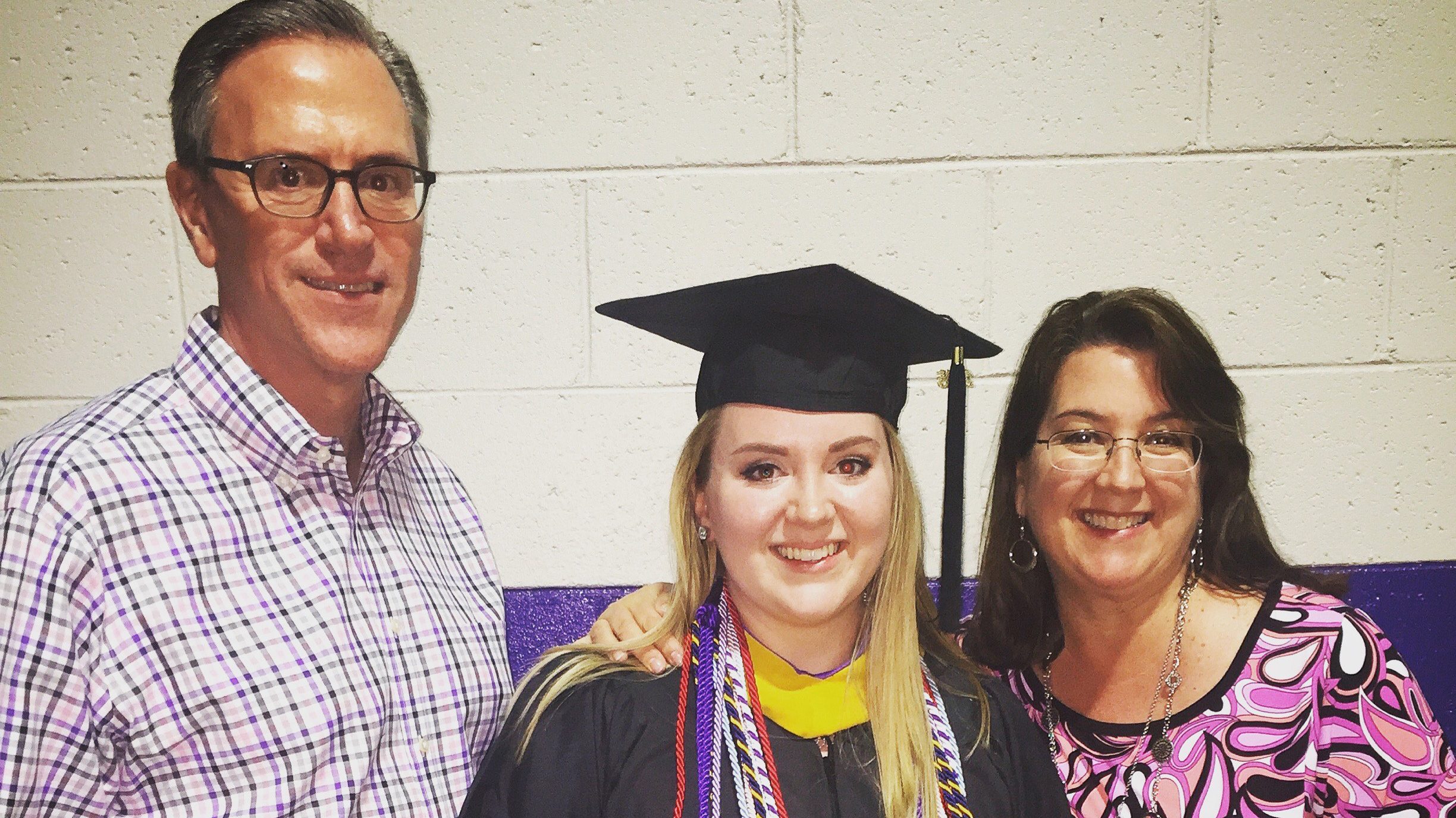 Photo of a woman in Furman graduation cap and gown with her dad on the left and her mom on the right.