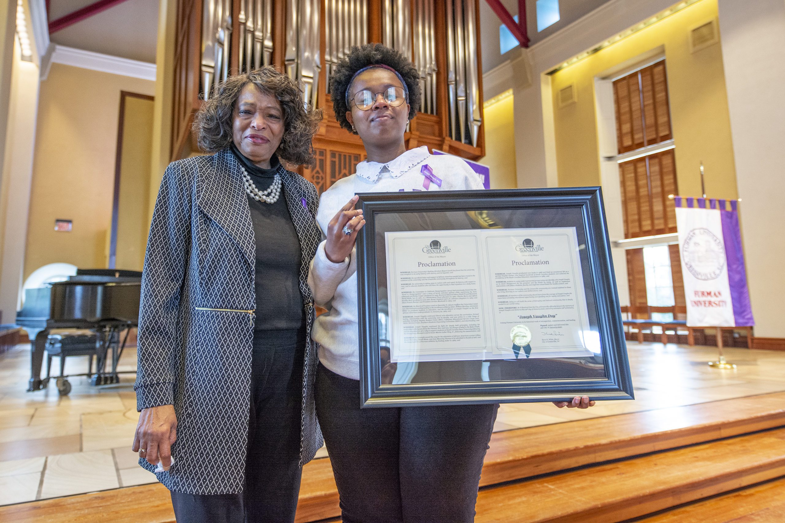 Adare Smith '20 holds a framed print of the city of Greenville's Joseph Vaughn Day Proclamation with Lillian Brock Flemming '71 to her left