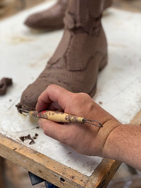 Close-up photo of a sculptor creating a shoe in clay.