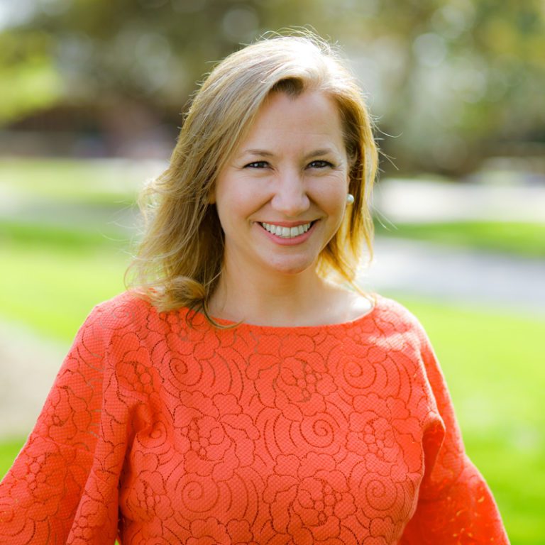 portrait taken outside of Rollins, wearing an orange top.