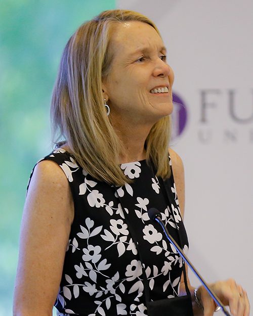 A smiling woman at a microphone looks out at a crowd of students