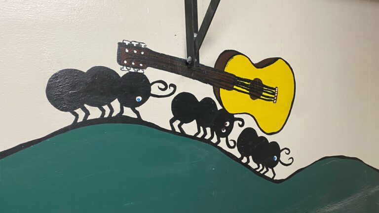 wall painting of three ants carrying an acoustic guitar on their backs
