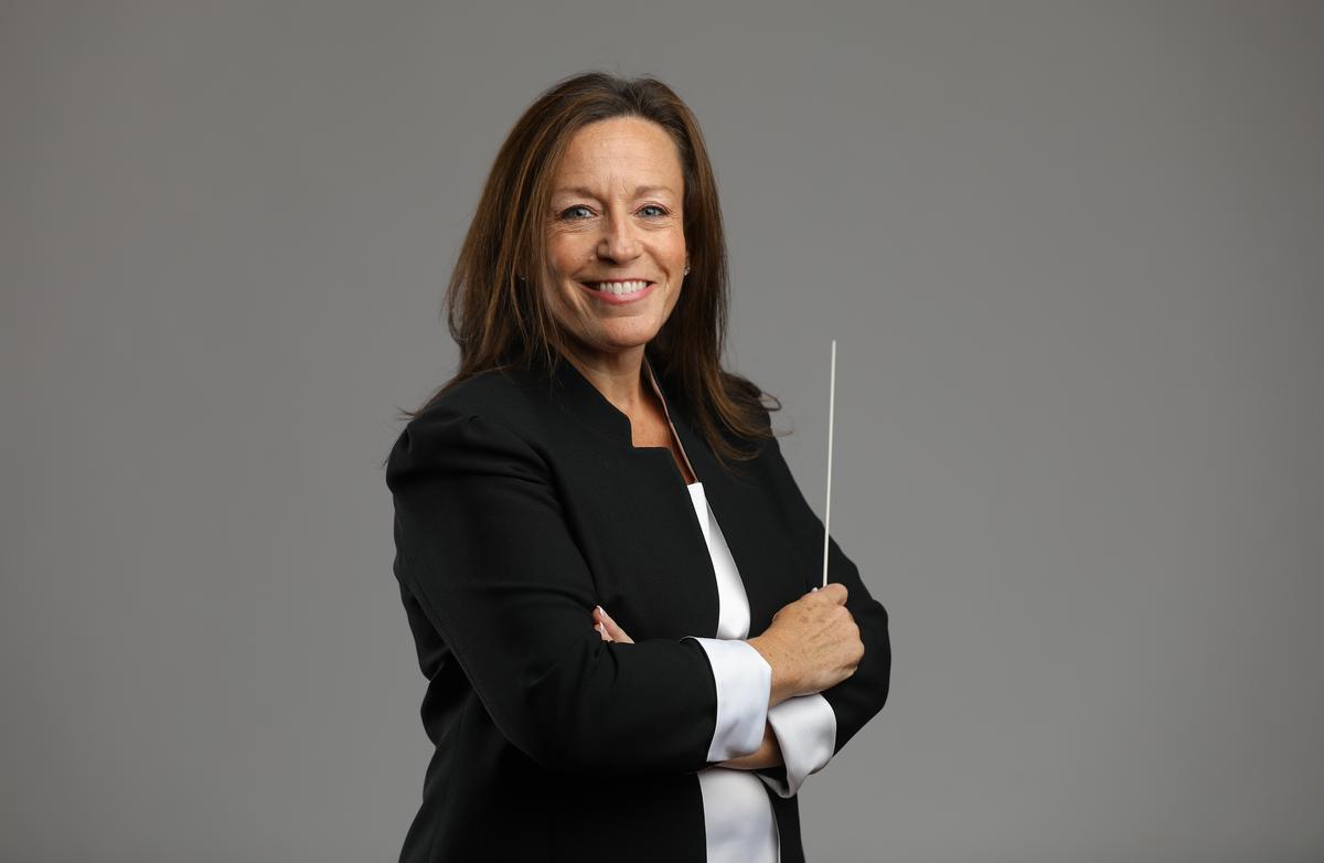 White woman with dark hair, holding a conductor's baton