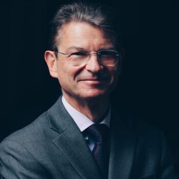 A white man wears glasses and gray suit in an indoor photo. David Gross.