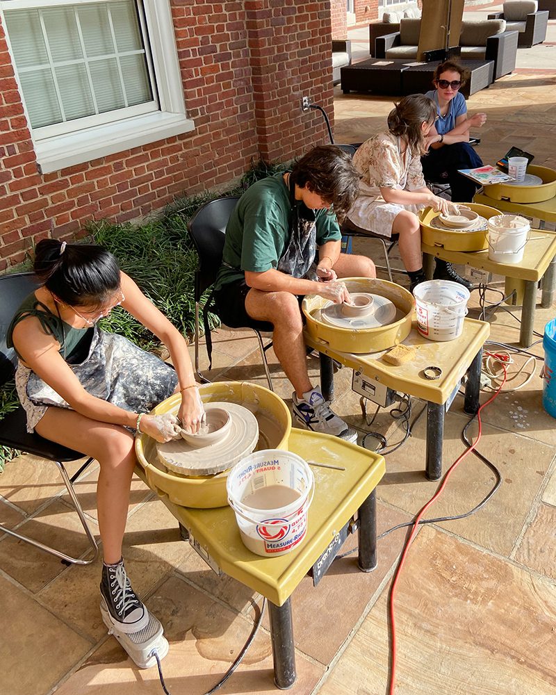 Four students sit at pottery wheels, heads bent over their creations.