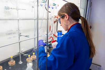 white woman in blue lab coat working with compounds in chemistry lab
