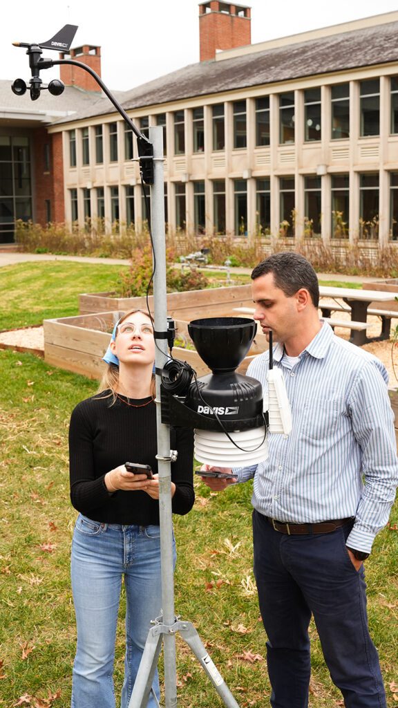 Two people stand with pole and equipment and operate a remote control while looking up.