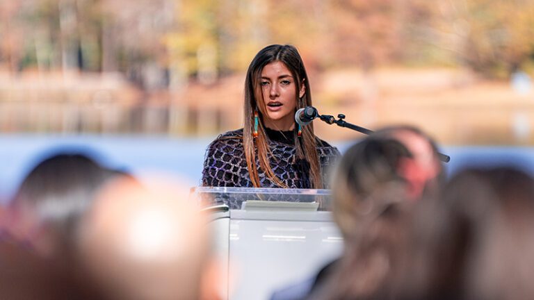 A woman speaks outside in front of a crowd. 