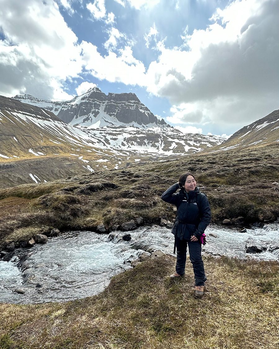 Woman in winter gear smiles against background of stream and mountain