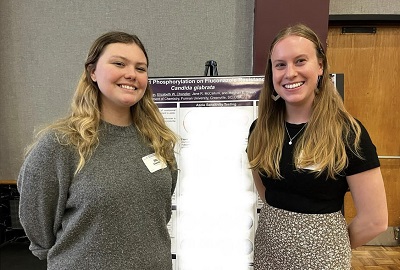 two white women stand in front of research poster