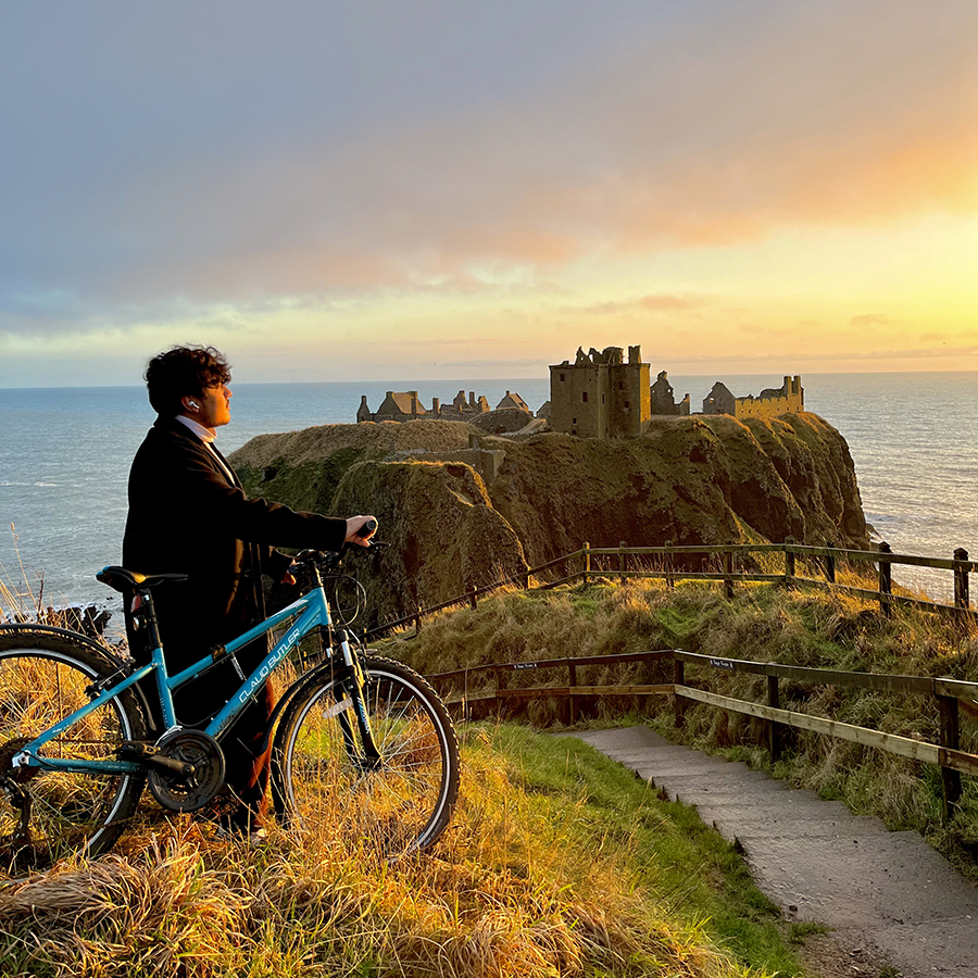 Man stands with bike with castle on the horizon